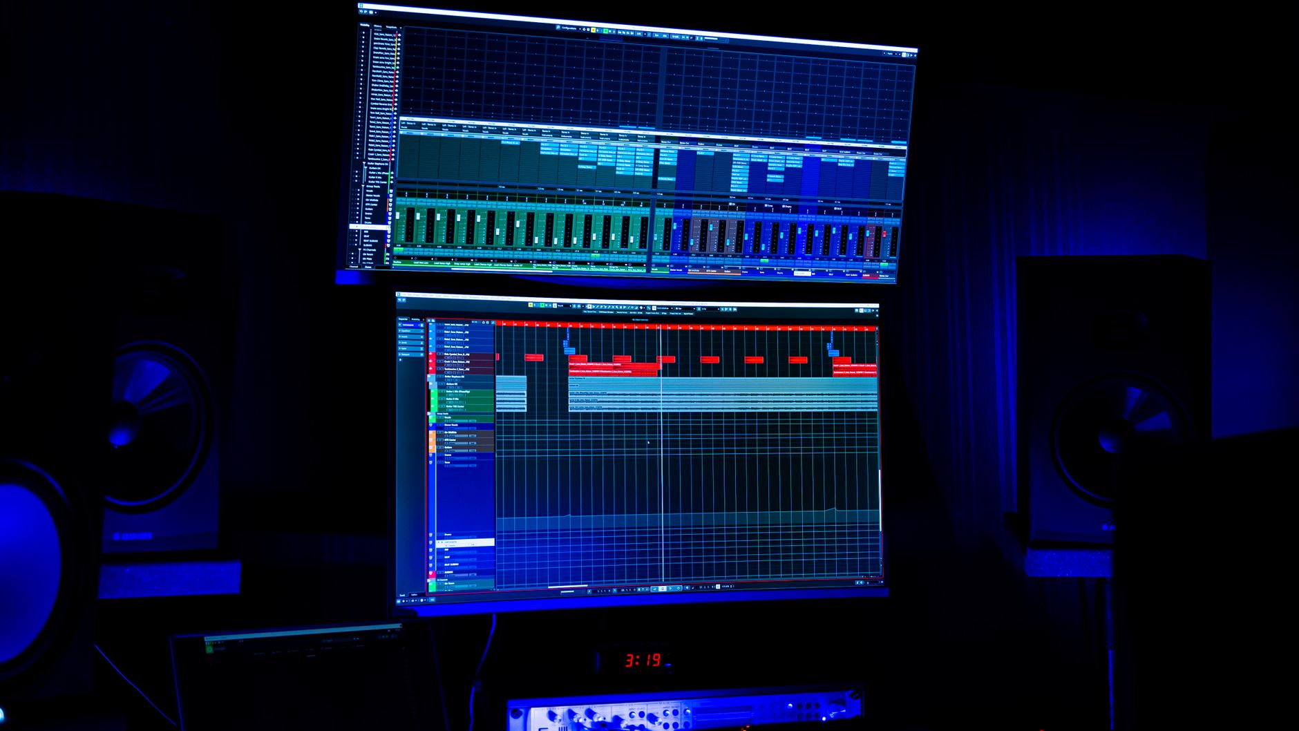 Recording studio with dual screens displaying audio editing software under blue neon lighting