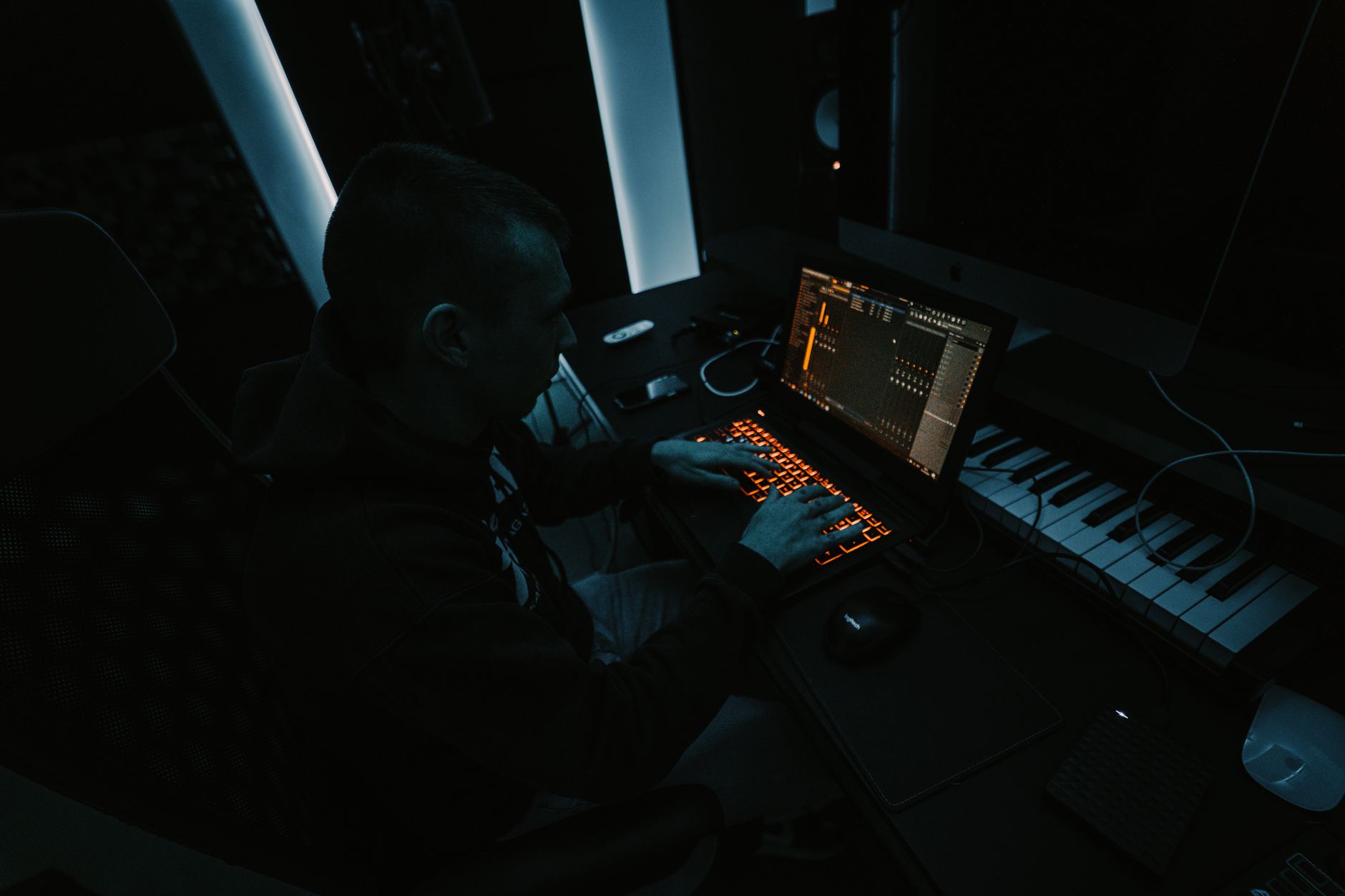 Music producer focused on composing tracks in a dimly lit studio with laptop and keyboard