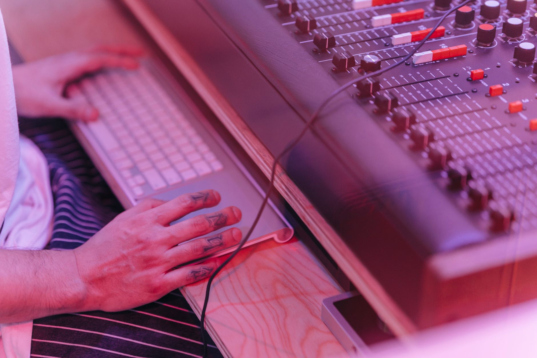Hands working at a sound mixer and keyboard in a recording studio